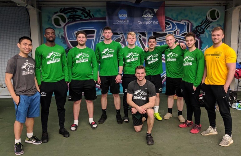 The SUNY Delhi men's tennis team following competing at the NAC Tournament, standing in front of the championship banner.